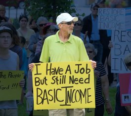 Man holding up sign that reads: I have a job but still Basic Income