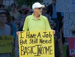 Man holding sign that says: I have a job but still need Basic Income